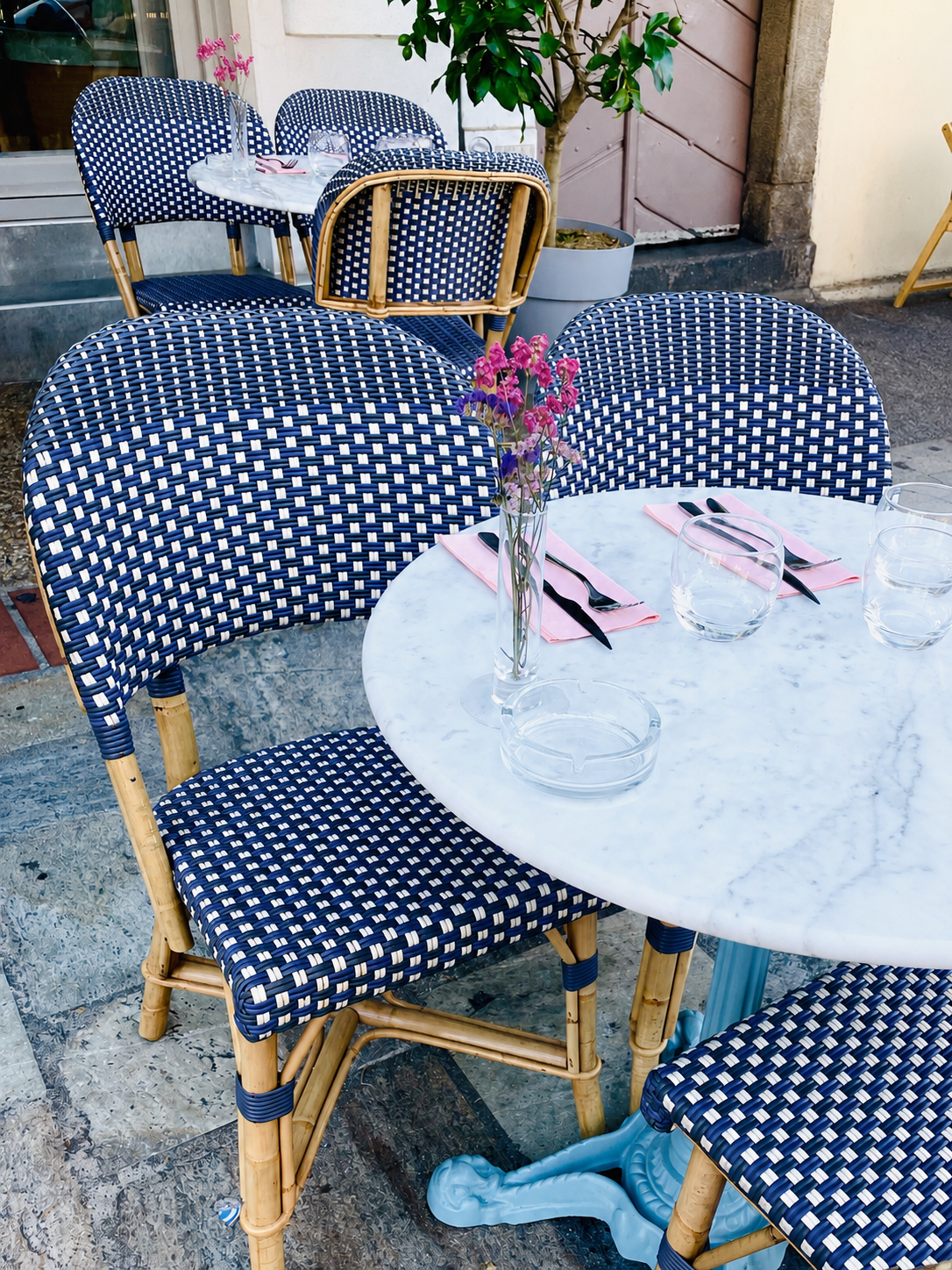 Bistro table with marble top and blue woven chairs on a sunny sidewalk